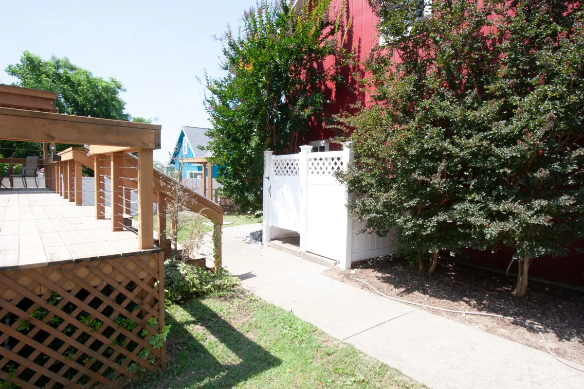 This image features a wooden deck bordered by a crisp white fence and surrounded by lush greenery. The fenced yard is visible, signaling a secure and open area suitable for pets to roam freely. The cheerful mood and ample space also suggest a welcoming environment for outdoor activities and gatherings.