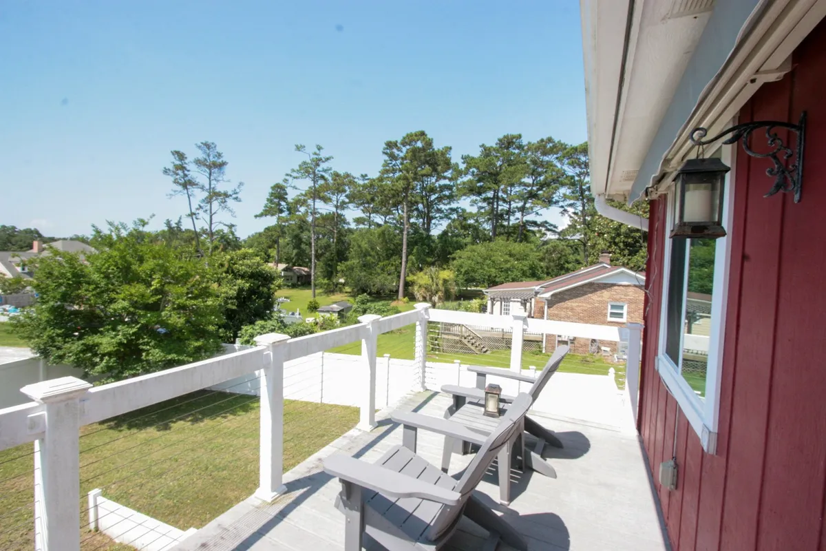A spacious wooden deck with outdoor seating overlooks lush green trees and the distant horizon. The scene captures the tranquil ocean breeze, inviting guests to relax, socialize, or watch the sunset together.