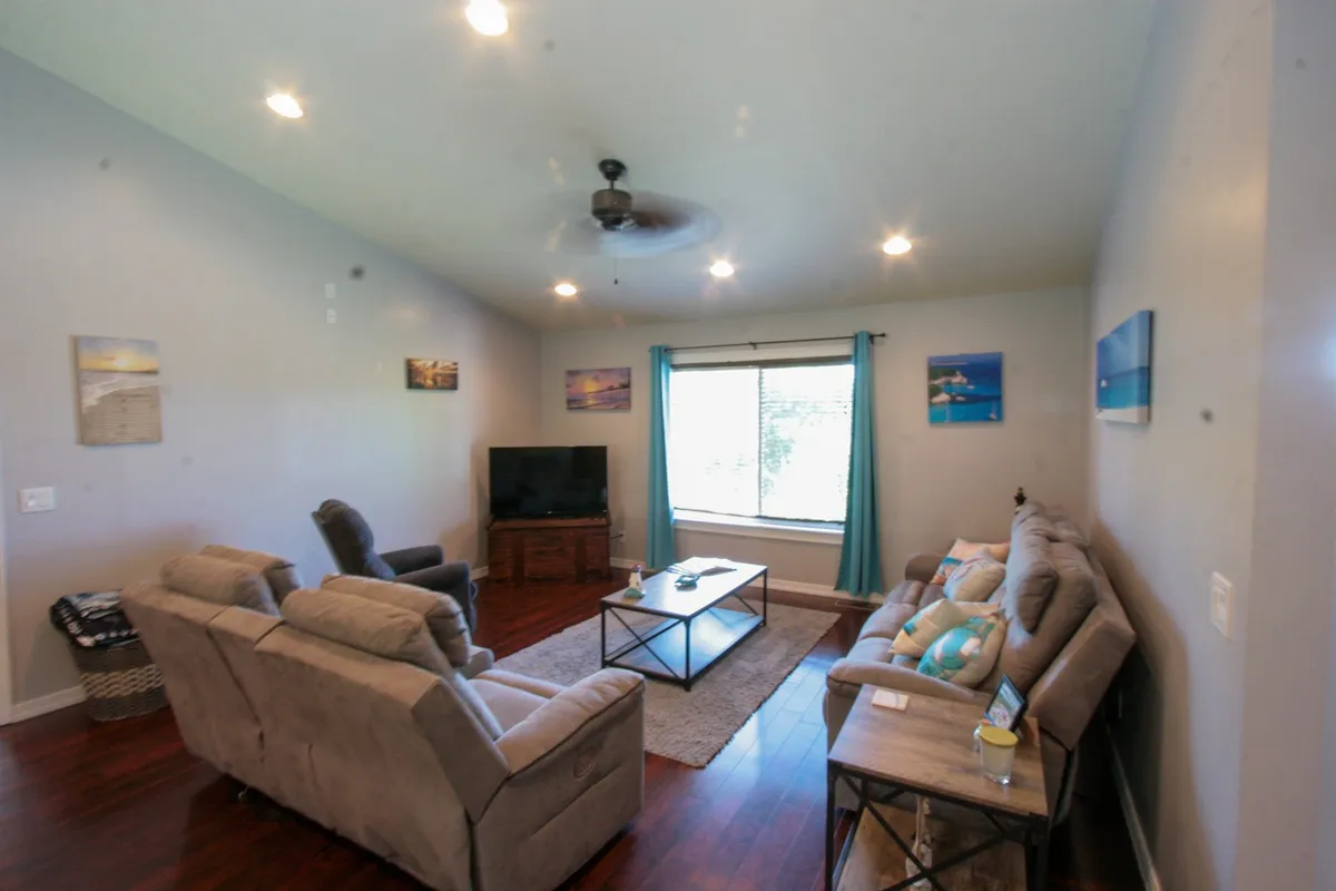 A cozy and welcoming seating area is bathed in natural light from a large window, with comfortable chairs and a sofa arranged for conversation or family gatherings. Decorative wall art adds a touch of personality, and the space invites relaxation, socializing, or watching TV together.