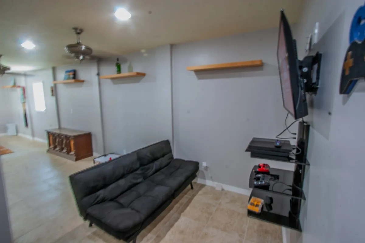 The living area features a sleek black sofa, a wall-mounted smart TV, and shelves adorned with tasteful decor. This setup encourages relaxation, entertainment, and group activities such as watching movies or playing games.