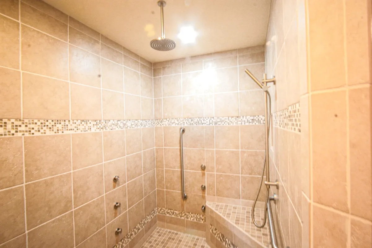 Close view of a walk-in shower with mosaic tile border, grab bars, and a modern showerhead. The shower area appears accessible and luxurious, suggesting both comfort and style.